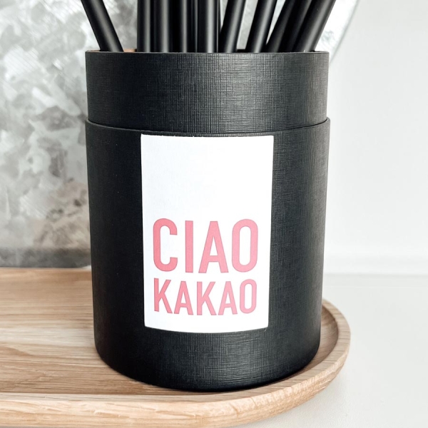 schwarze Pappdose mit Deckel in einer hochwertigen Leinenstrucktur mit weißen Etikett und der Aufschrift "ciao kakao" in einem sommerlichen Pink. Auf dem Bild ist eine Magnettafel zu sehen und passende Bleistifte der Marke FRAULENZA.IN. Abgebildet ist auc